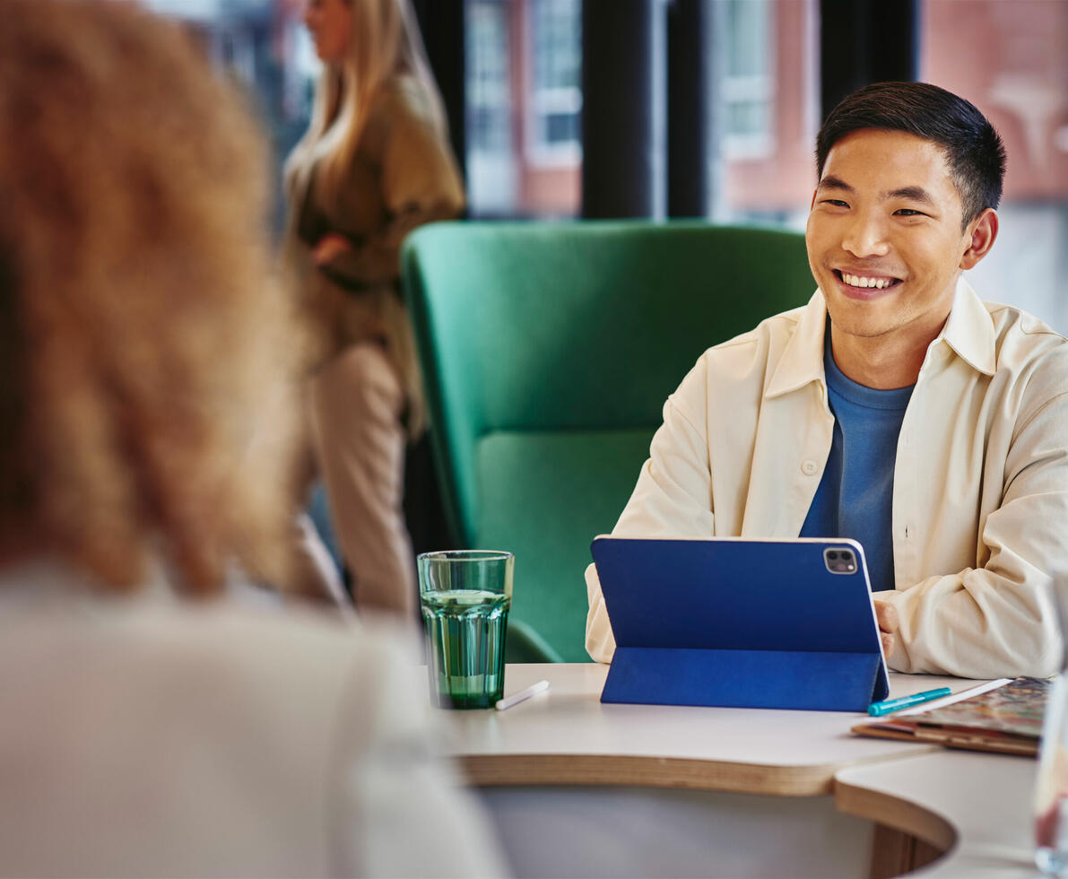Male smiling, sitting on a table behind his tablet Male smiling, sitting on a table behind his tablet
